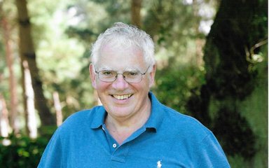 Chris Simpson smiling and standing in front of a wooded area in the sunshine