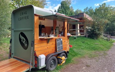 Mobile coffee trailer with wooden cladding and open serving hatches, parked on grass.