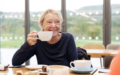 A smiling customer sitting in front of the cafe windows holding up a drink 