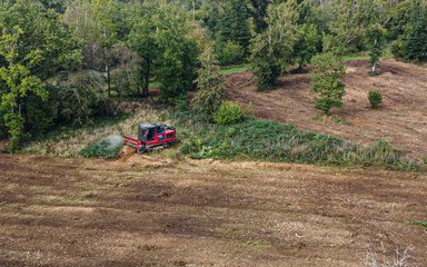 A large forestry machine called a mulcher churns up vegetation on the ground leaving behind brown soil. 