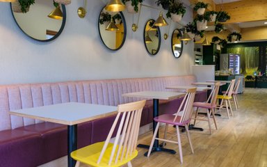 A cafe with pink bench seating and yellow and pink chairs
