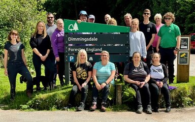 group of people stood around Dimmingsdale Forest sign in a forest