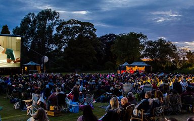 A crowd sit down in the forest in front of a large outdoor cinema screen to enjoy the film Dirty Dancing