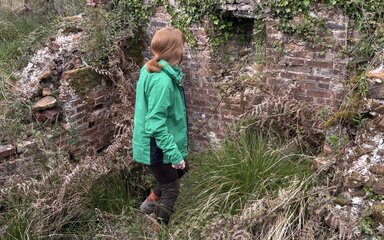 Woman in green jacket standing by a wall.
