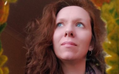 A woman with mid-length brown wavy hair stares up to her right, looking in deep thought. She has piercing blue eyes and wears a purple floral scarf