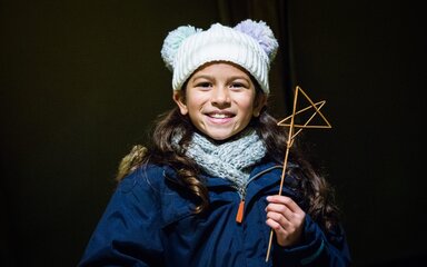 A young girl holds up a wooden stick star that she has created 