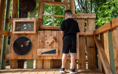 Seen from behind, a young boy playing in an interactive wooden play area.