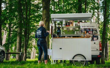 A coffee trailer and staff member standing under the trees.