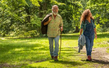 A woman and a man walking through the green sun lit forest looking up