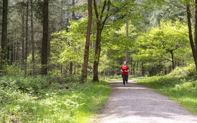Woman running along trail towards the camera through trees