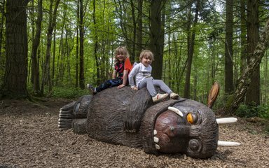 Two children sitting on a Gruffalo sculpture