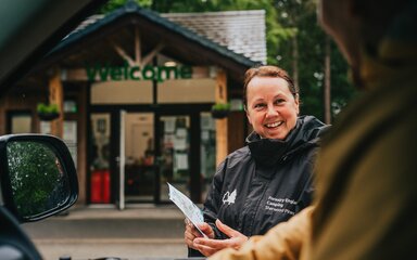A smiling woman wearing Forestry England branded uniform, seen through a open car window.
