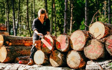 A woman in Forestry England uniform smiling as she stands by a log pile with a tape measure.