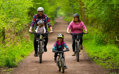 Family of four cycle down a forest path