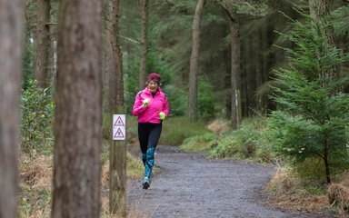 A woman in running clothes and a pink hat running along a forest path in winter