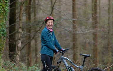 Older woman stood by a bike in a forest
