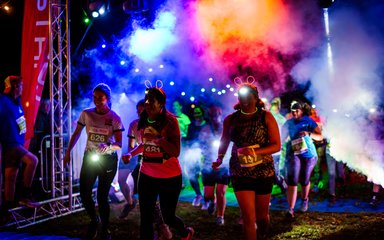 Women running in the dark with light up ears on lit by colourful lights