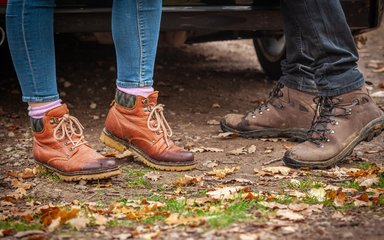Close-up of two people's walking boots stood on forest ground.