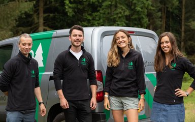 Group of Forestry England staff stood smiling in front of grey Forestry England van