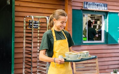 A lady carrying a tray of hot drinks 