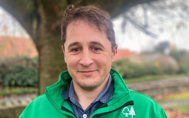 Man in green jacket stood next to a tree