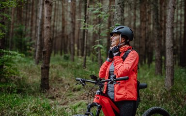 Woman biker putting on cycling helmet in forest
