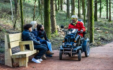 Family sitting on a bench in a forest, the dad is in a mobility scooter