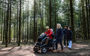A family walking in the forest, the dad is using a mobility scooter.
