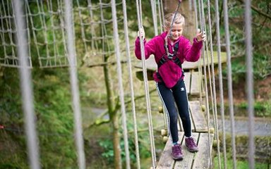 A girl wearing a harness, on part of a Go Ape treetop course