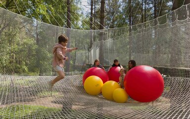 Four children and an adult in the Nets enclosure with large red and yellow inflatable balls