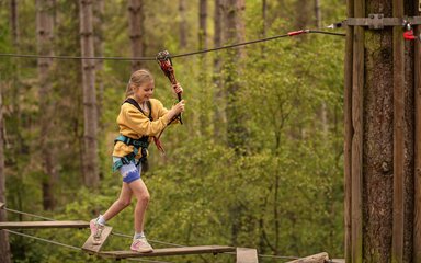 A young girl on a high-ropes course in the trees.