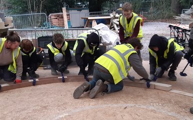 Young boys kneel down clamping pieces of wood together to create an arch.