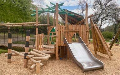 A woodland play area with balance beams and a slide