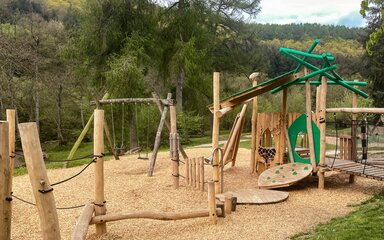 A woodland play area with balance beams, a small climbing wall and swings.