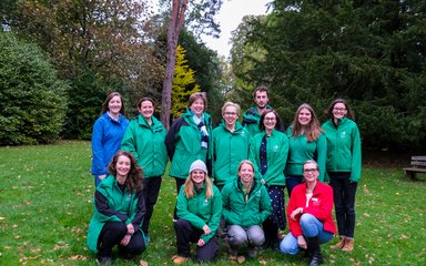 A group of people smiling at the camera on the grass with trees in the background