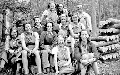 A group of women in the forest in front of a timber stack