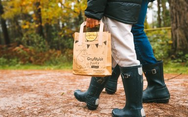 Shot of legs and wellies of two people walking through forest holding Gruffalo paper bag
