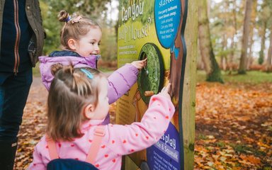Two young children interacting with a Gruffalo activity in a forest