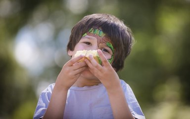 Boy with Gruffalo face paint eating a piece of cake