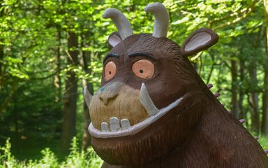 A headshot of a wooden Gruffalo sculpture in a forest