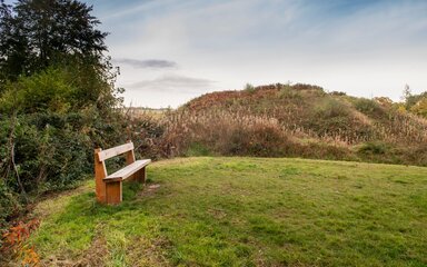 A wooden bench on a grassy clearing with hills behind.