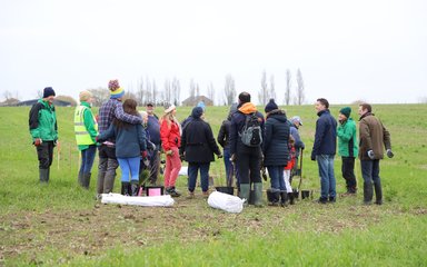 A small crowd of people wearing warm outdoor clothing stand in a group with tree planting equipment