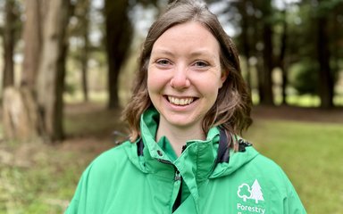 A woman in a green jacket smiling in the forest