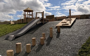 A playground of wood structures at the top of a small hill with a slide running down the hill