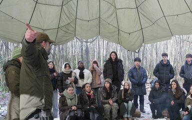 Still from Into the Forest film - showing a group of people sat under canvas in the forest