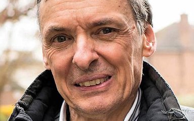 A man with dark grey hair smiles at the camera