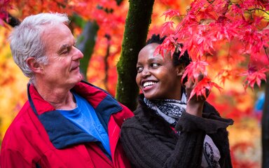 A man and woman smile at each other looking at a red maple tree