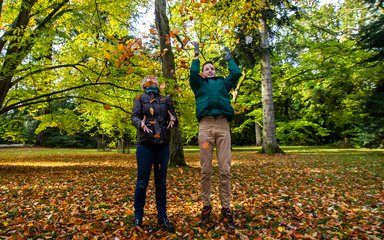 A young man and his mum throw loaves in to air in front of a beautiful landscape of yellow leaves.