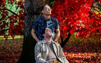 two men with eyes shut in a sunbeam, with a red tree behind them