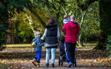 A family walk away from the camera with a baby in the fathers arms and a young boy looking behind him with mum holding the reins.